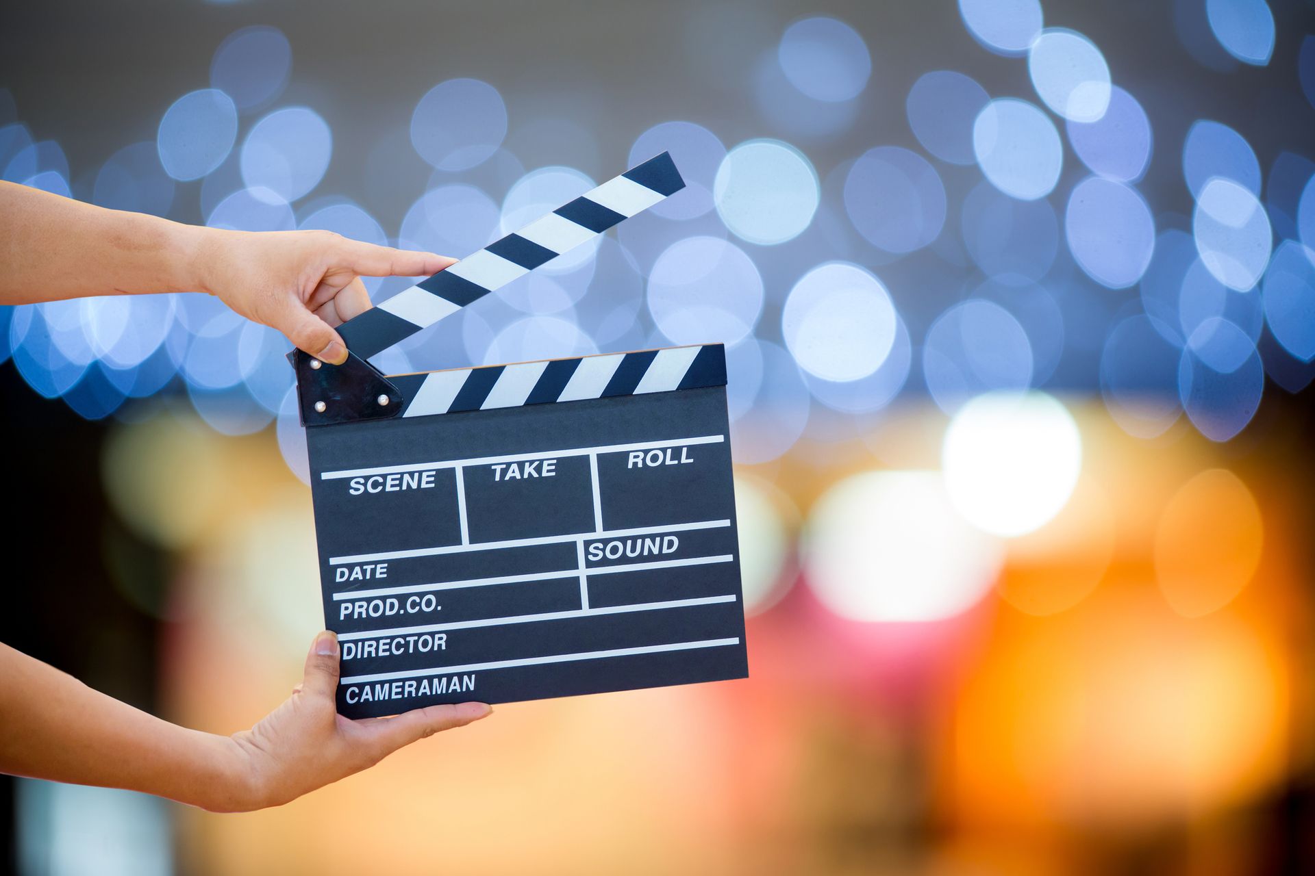 Hands holding a film clapperboard against a blurred blue and orange light background